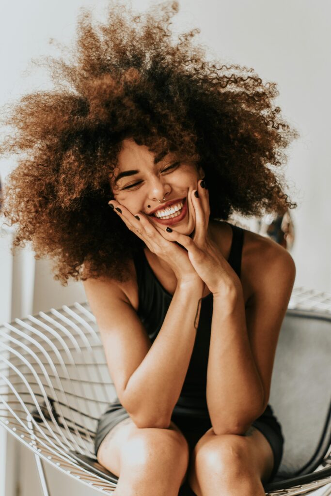 A cheerful woman with an afro hairstyle sitting indoors, showcasing happiness and style.