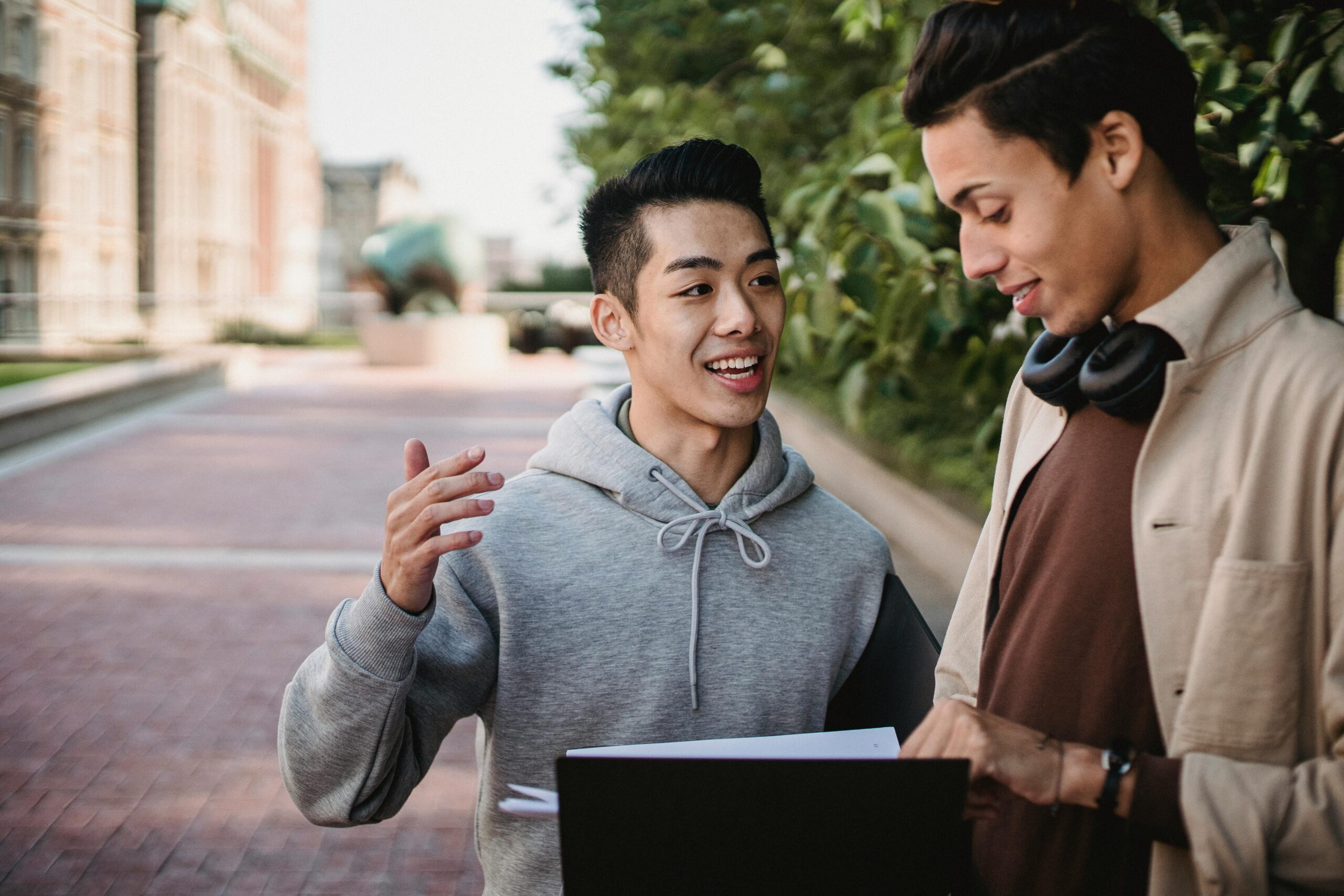 Two young men engaging in conversation outdoors on a sunny college campus walkway.