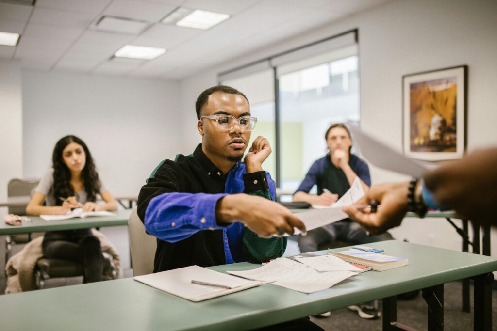 College students sitting in a classroom receiving papers, focused on studies and assignments.