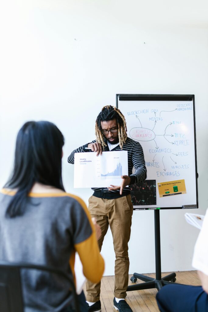 A diverse group engaged in a cryptocurrency lesson with charts and a whiteboard presentation.